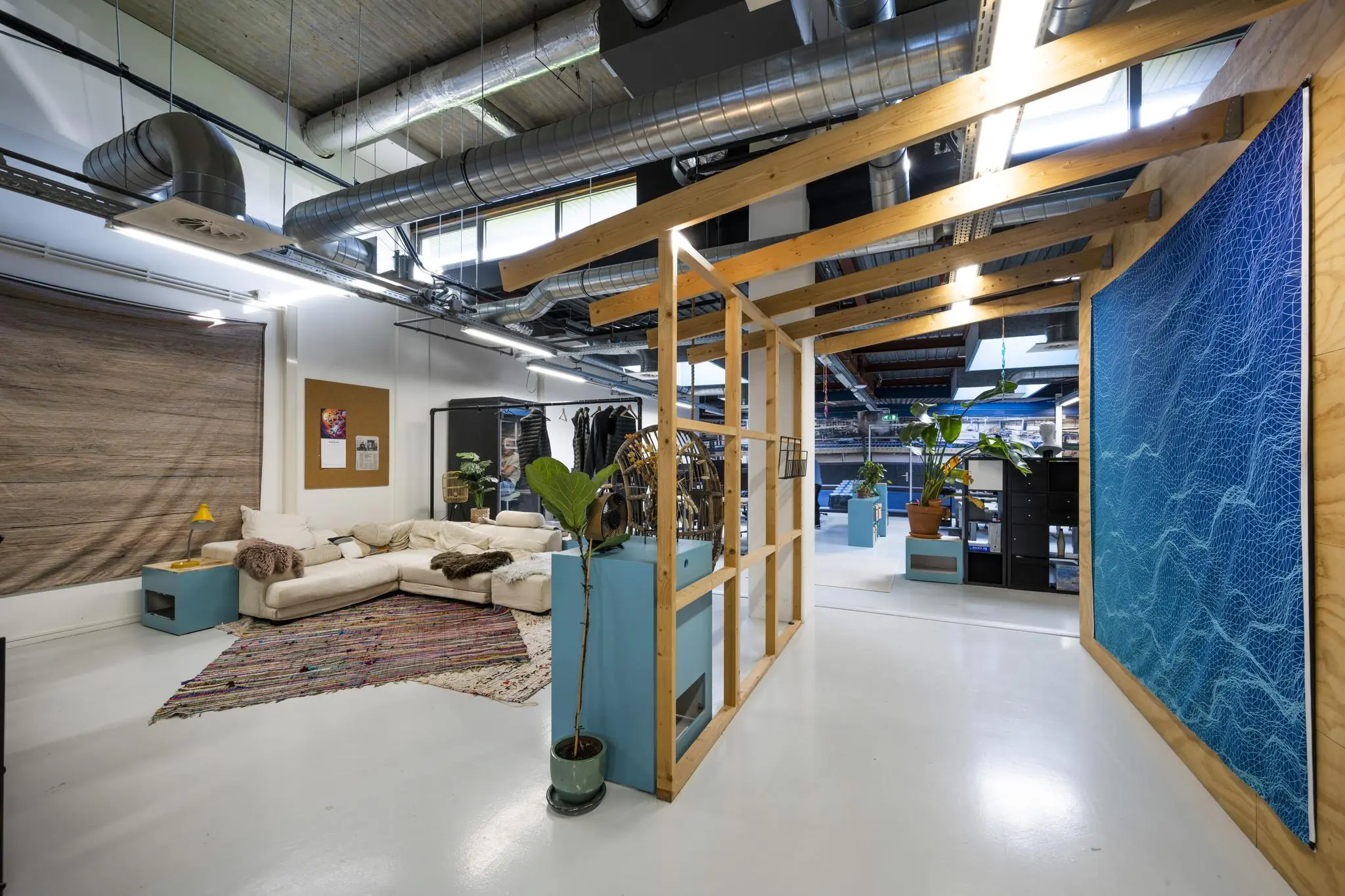 Modern ingericht kantoor aan de Joan Muyskenweg met loungehoek, industriële plafonddetails en planten.